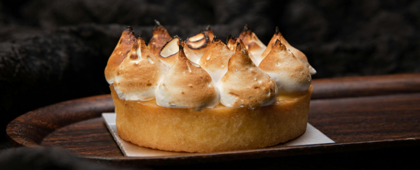 A cake with flamed creme topping on a wooden platter.
